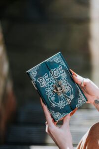 Crop anonymous female with vintage magic diary in manicured hands on blurred background in daytime